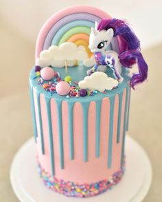 a pink and blue cake with a rainbow pony on it's icing, surrounded by sprinkles