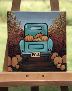 a painting of a blue truck with pumpkins on the front and back, sitting on a wooden easel