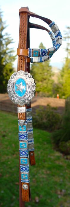 a horse bridle with a blue and white design on the top is attached to a wooden pole