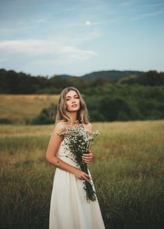 a woman standing in a field holding a bouquet of flowers