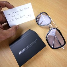 a person holding up a note next to some glasses on a wooden table with a card in front of them