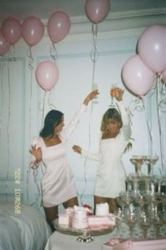 two women standing in front of a table with pink balloons