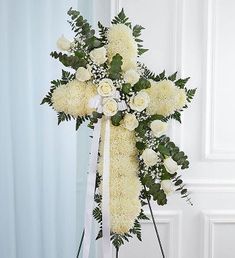 a cross with white flowers and greenery on the top is in front of a wall