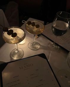 two martinis are sitting next to each other on a table with menus and wine glasses