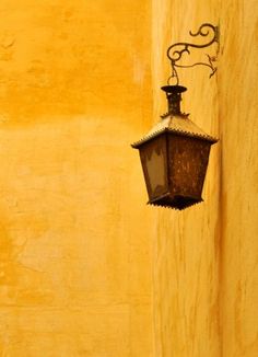 an old fashioned street light hanging from the side of a building on a yellow wall