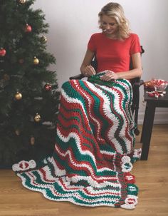 a woman is holding up a crocheted christmas blanket