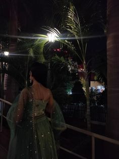 a woman in a green dress standing on a balcony at night with palm trees behind her