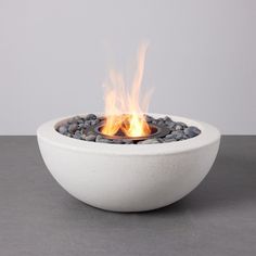 a white bowl filled with rocks and fire on top of a gray table next to a wall