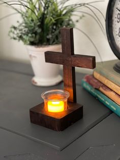 a candle is lit in front of a cross on a table next to books and a potted plant