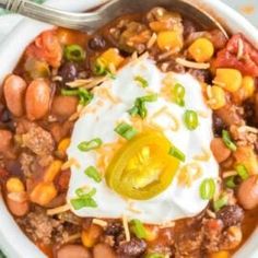 a white bowl filled with beans, corn and sour cream on top of a green table cloth