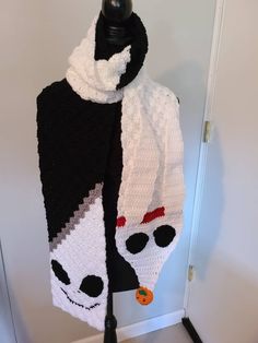 a black and white knitted scarf with skulls on the front, one skull is wearing a red bow