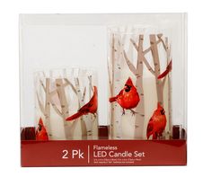 two glass candles with red birds on them in front of white birch tree trunks and branches