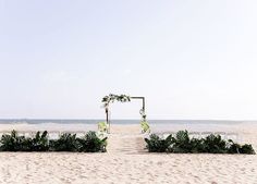 an outdoor ceremony set up on the beach with greenery and flowers in the foreground