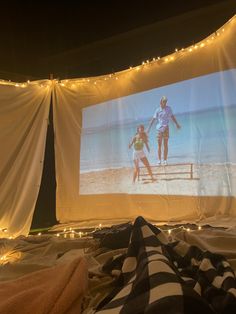 an outdoor movie screen with lights on the sides and two people playing in the water