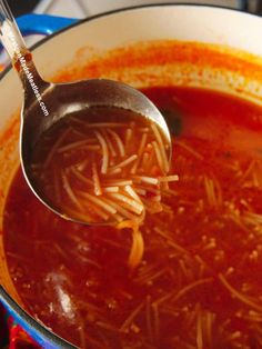 a ladle full of tomato soup with noodles in it