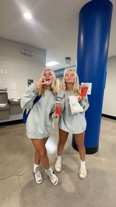 two women standing next to each other in front of a large blue column holding drinks