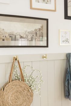 a basket hanging on the wall next to a coat rack with flowers and pictures above it