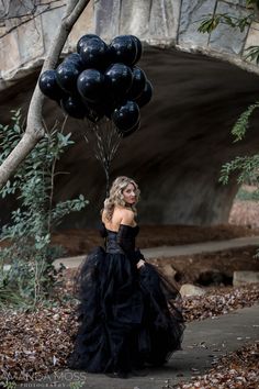 a woman in a black dress is holding some balloons