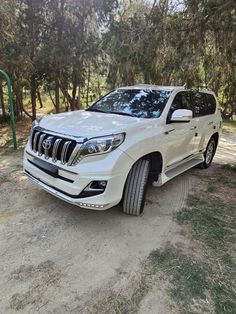 a white suv parked in front of some trees on a dirt road with no one around it