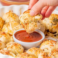 a person dipping sauce onto some bread rolls