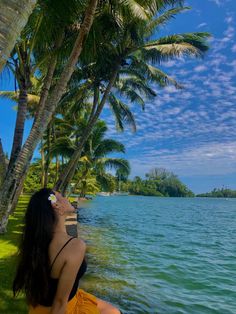 a woman sitting on the edge of a body of water next to trees and grass