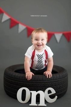 a baby in a tie and suspenders is sitting on a tire with the word one