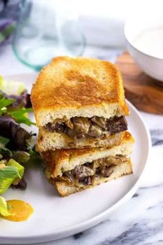 a sandwich cut in half sitting on top of a white plate next to a salad