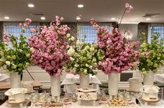 three tall vases filled with pink flowers on top of a table covered in food