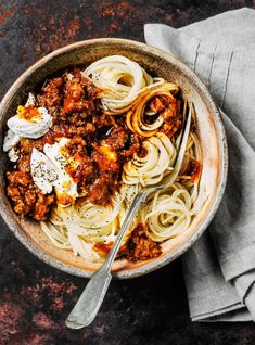 a bowl filled with spaghetti and meat sauce on top of a gray napkin next to a fork