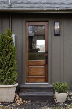 two potted plants are sitting in front of the door to a small gray house