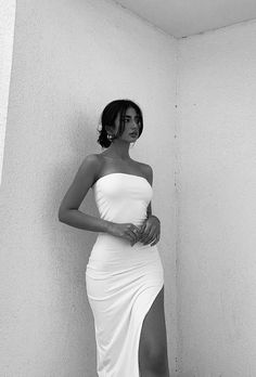 a woman in a white dress leaning against a wall