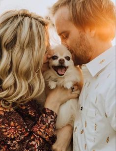 a man and woman are cuddling with a small dog in their arms as the sun shines down on them