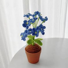 a crocheted pot with blue flowers in it on a table next to a white curtain