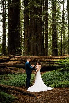 a bride and groom standing in the middle of a forest holding hands with each other