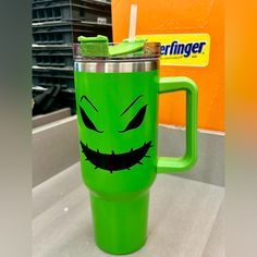 a green cup with a face drawn on it and a straw in front of an orange wall