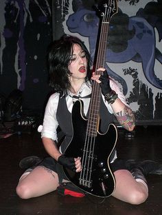 a woman with black hair and piercings holding a guitar