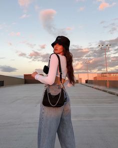 a woman standing in an empty parking lot with her handbag on her hip and looking at the sky