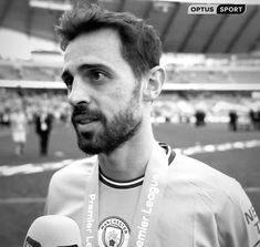 a man holding a microphone standing in front of a soccer field