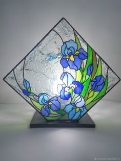 a stained glass vase sitting on top of a wooden stand with blue flowers in it