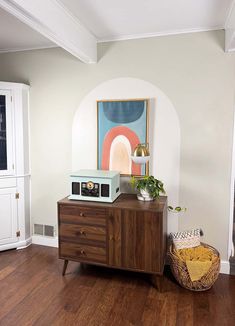 a microwave on top of a wooden cabinet in a room with white walls and wood floors