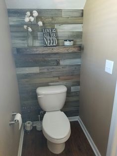 a white toilet sitting inside of a bathroom next to a wooden paneled accent wall