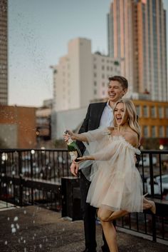 a man and woman standing next to each other in front of tall buildings with rain falling on them