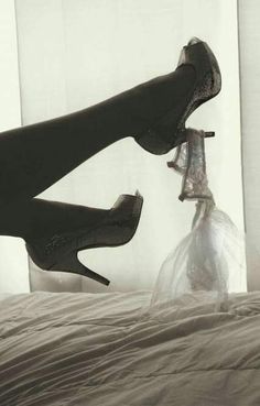 black and white photograph of woman's legs with high heels on top of bed