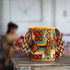 Bold patterns in orange brown blue and white are captivating in this hand-crocheted acrylic bucket bag or mochila. Working to preserve their cultural identity and artisanal traditions artisans of the Wayuu Community create the shoulder bag. The Wayuu are an indigenous people located on the Guajira Peninsula in northern Colombia. Legend has it that a spider named Wale Keru taught a Wayuu woman how to weave and crochet. The unlined shoulder bag closes with a tassel-accented drawstring. How To Weave, Caribbean Culture, Amazing Crochet, Wayuu Bag, Woven Handbags, Cultural Identity, Bold Patterns, Indigenous People, Crochet Tapestry