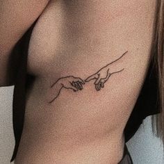 a woman's chest with the creation of hands tattoo on her left side ribcage