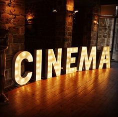 the word cinema is lit up in front of a brick wall with lights on it