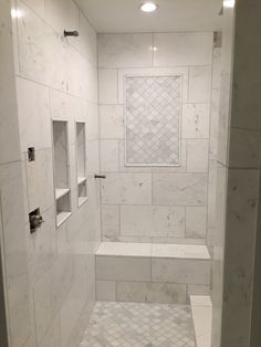 a walk in shower sitting next to a white tiled wall with shelves on each side