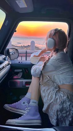 a woman sitting in the passenger seat of a car with headphones on and looking out at the ocean