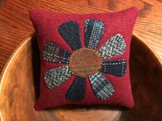 a red pillow with a flower on it sitting on top of a wooden table next to a bowl