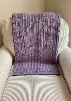 a purple knitted blanket sitting on top of a white couch next to a pillow